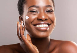 Woman applying moisturizer onto her cheek and smiling.