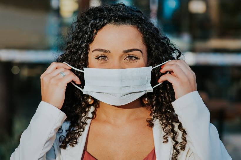 Woman with curly hair putting on her protective mask