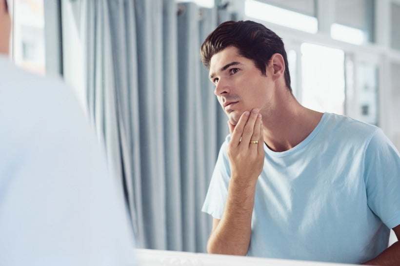 Man touching his chin and looking into a mirror.