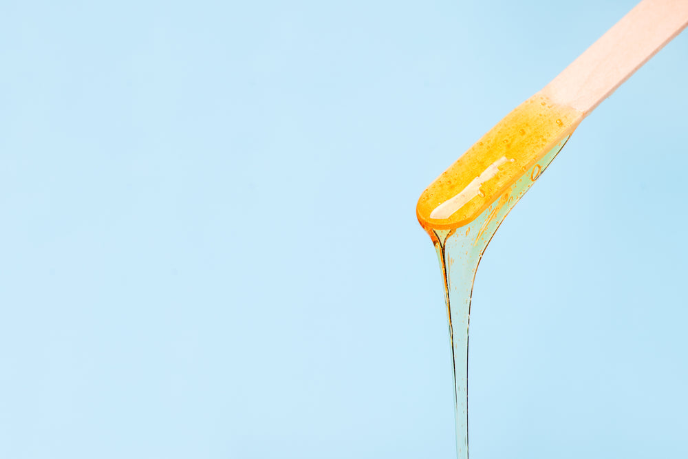 Wax applicator with wax dripping on a baby blue background