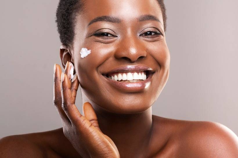 Woman applying moisturizer onto her cheek and smiling.