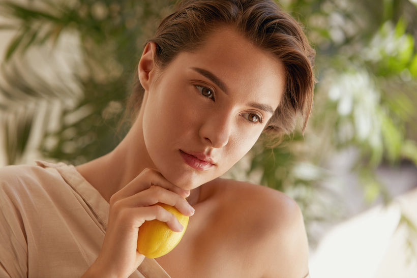 Woman holding a lemon slice in one hand, with her thumb pointing down with the other