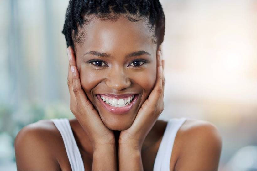 Woman with her hands framing her face and smiling while looking into the camera.